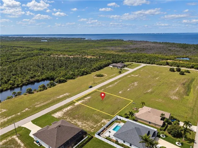 Expansive cleared lot with surrounding green space, paved road frontage, and distant water
