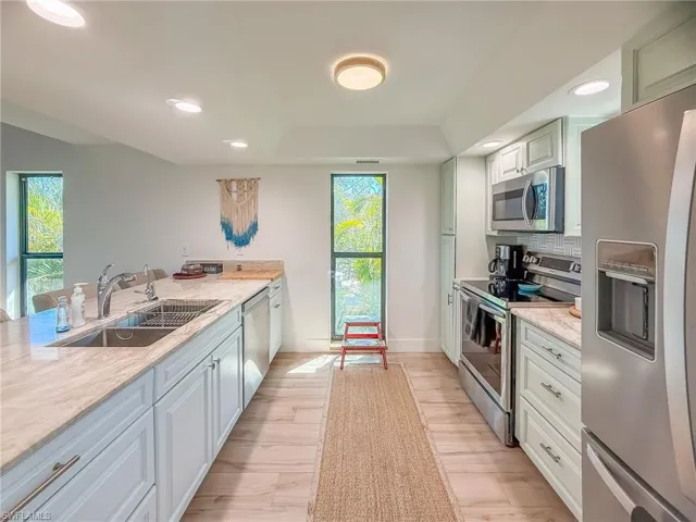 Kitchen with sink, backsplash, light stone counters, stainless steel appliances, and light hardwood / wood-style flooring