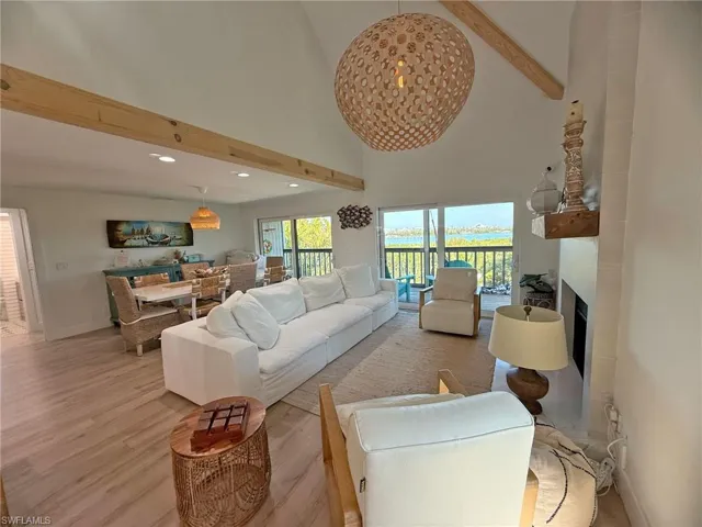 Living room featuring light hardwood / wood-style flooring, a large fireplace, beamed ceiling, and a high ceiling