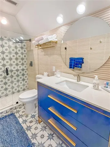 Bathroom with vanity, toilet, a shower with door, and vaulted ceiling