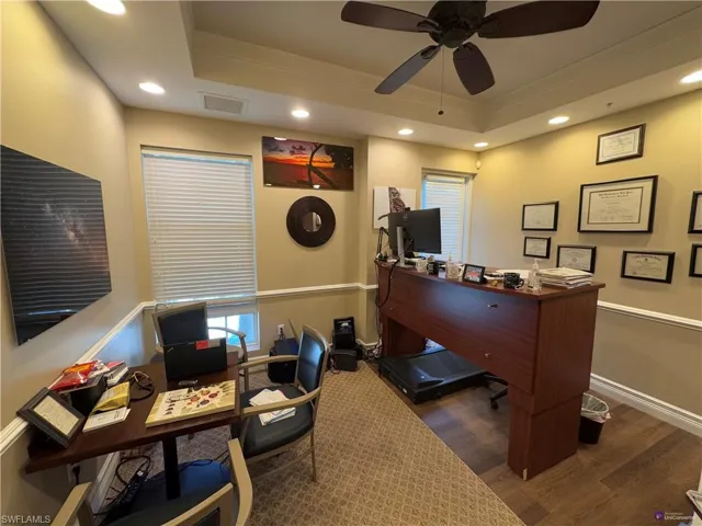 Office space featuring ornamental molding, a raised ceiling, ceiling fan, and dark wood-type flooring