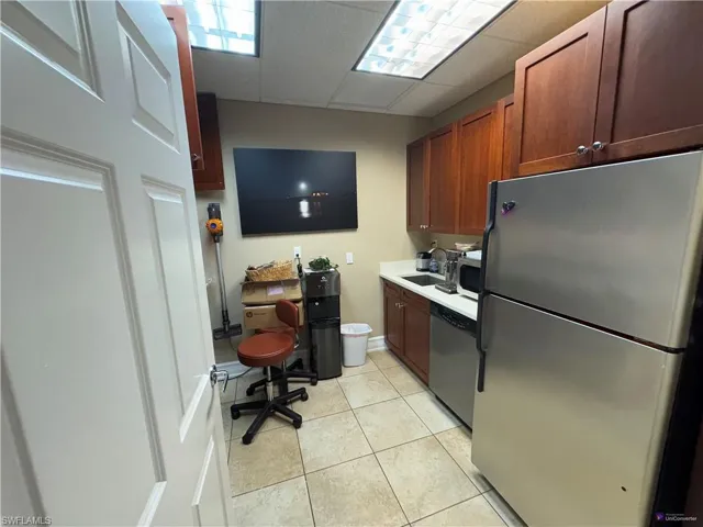 Kitchen with sink, light tile patterned floors, stainless steel appliances, and a drop ceiling