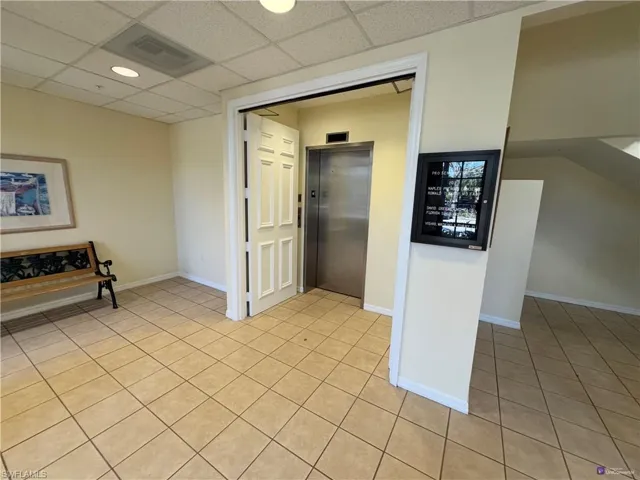Hallway featuring light tile patterned floors, elevator, and a drop ceiling