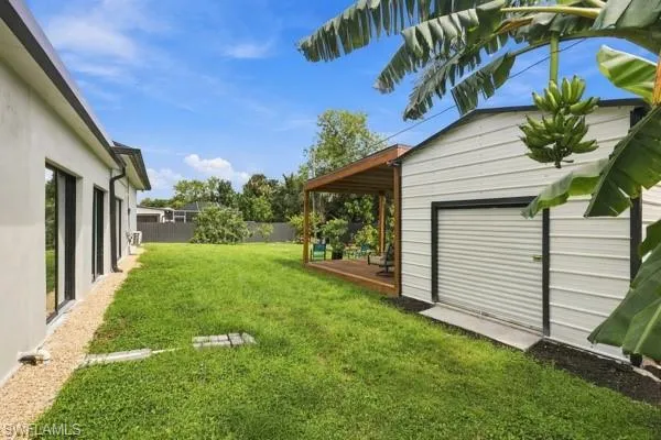 Expansive green lawn, white-sided structure with roll-up door, wood deck with pergola, and modern building exterior