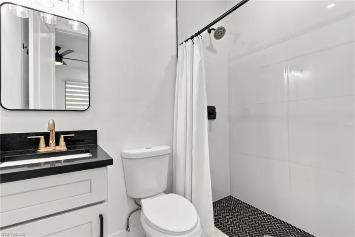 White vanity with dark countertop, rectangular sink, and gold-finish faucet