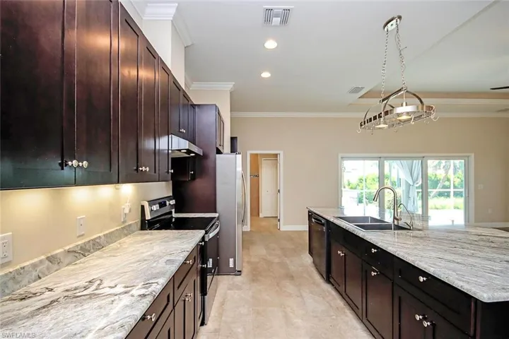 Kitchen with stainless steel appliances, crown molding, under cabinet range hood, dark brown cabinets, and light stone counters