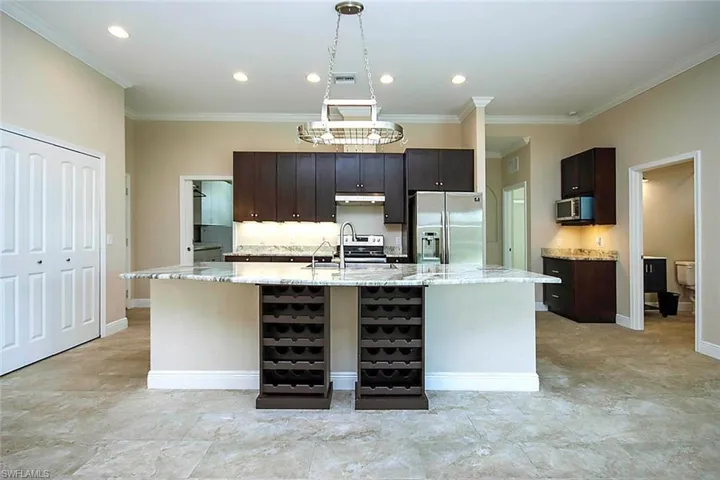 Kitchen with stainless steel appliances, a kitchen island with sink, ornamental molding, light stone countertops, and under cabinet range hood