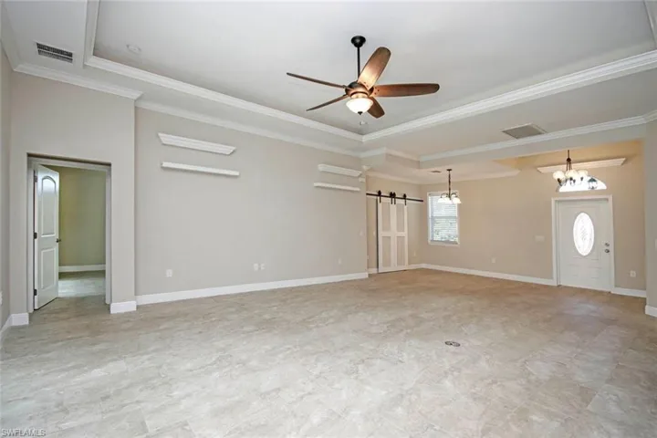 Unfurnished living room featuring a barn door, ceiling fan, crown molding, and a chandelier