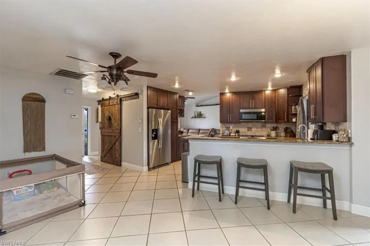 Kitchen featuring a barn door, stainless steel appliances, a kitchen bar, ceiling fan, and dark brown cabinetry