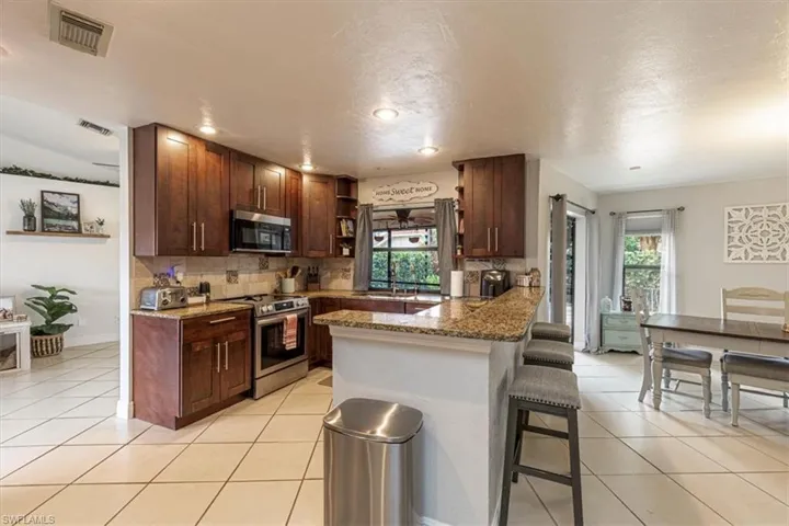 Kitchen featuring appliances with stainless steel finishes, light stone counters, a kitchen breakfast bar, tasteful backsplash, and healthy amount of natural light