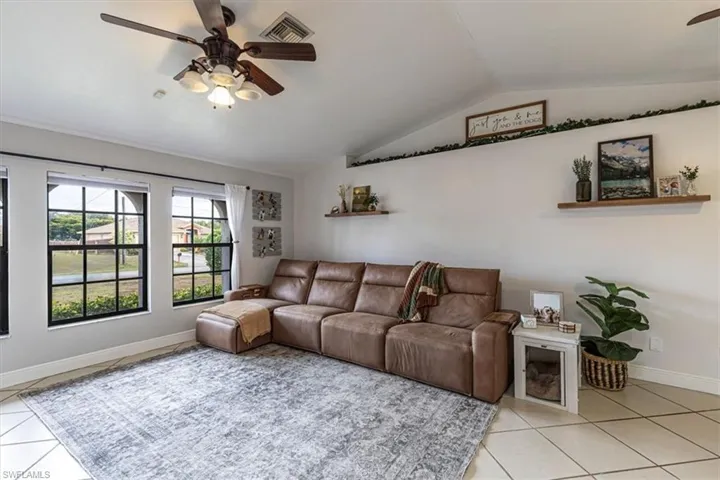 Living room with ceiling fan, light tile patterned floors, and vaulted ceiling
