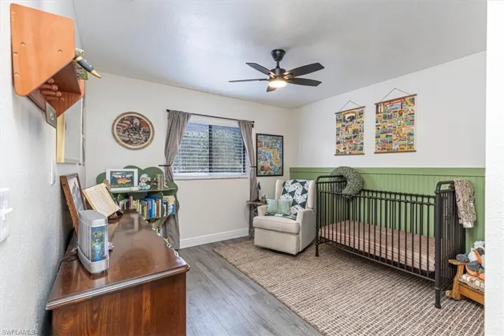 Bedroom with a nursery area, wood finished floors, and a ceiling fan