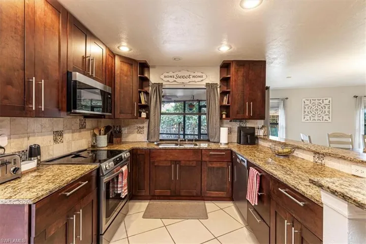 Kitchen with stainless steel appliances, dark brown cabinetry, light stone countertops, decorative backsplash, and plenty of natural light