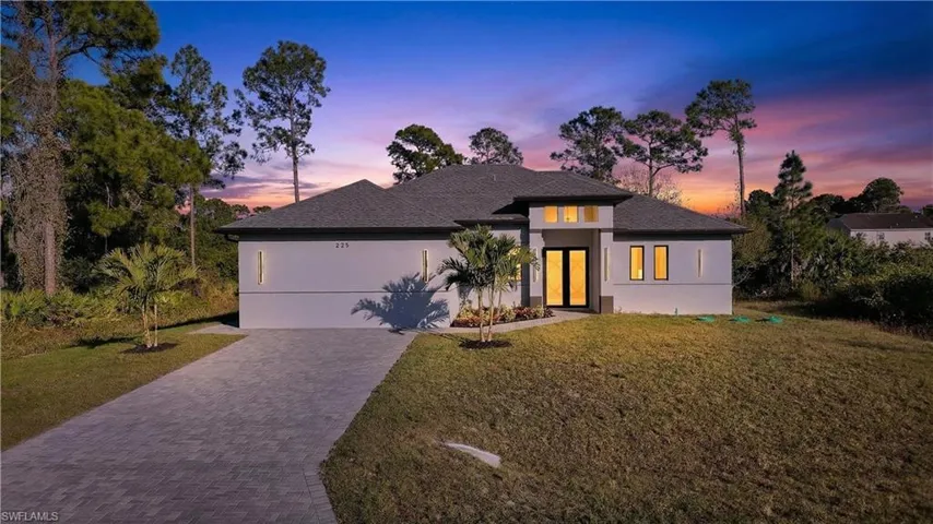 Prairie-style home with stucco siding, a front lawn, driveway, roof with shingles, and a garage