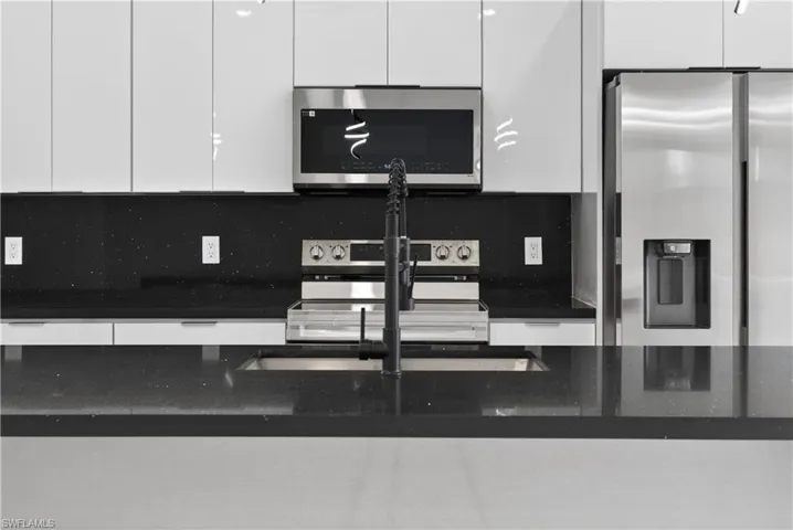 Kitchen with open floor plan, dark countertops, a center island with sink, white cabinets, and stainless steel appliances