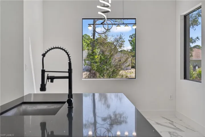 Kitchen with dark stone counters, hanging light fixtures, ceiling fan, open floor plan, and a tray ceiling