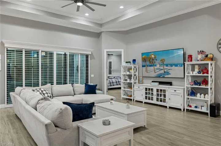 Living room with light hardwood / wood-style floors, a towering ceiling, a raised ceiling, ceiling fan, and ornamental molding