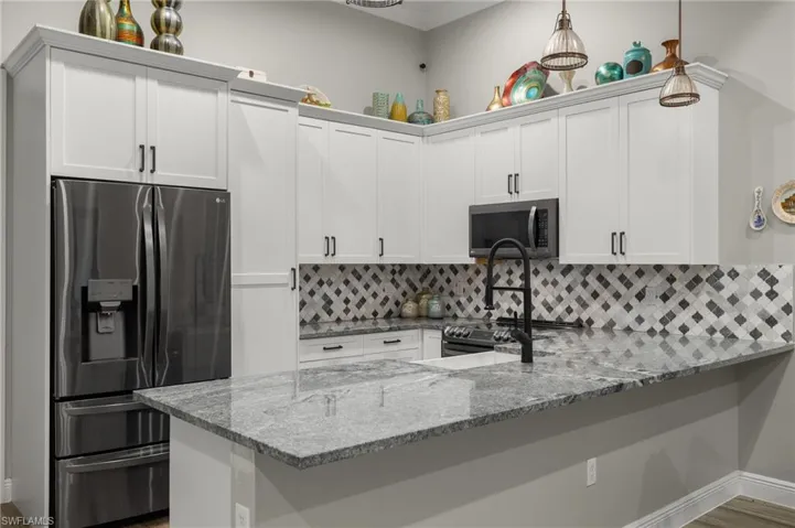 Kitchen with white cabinetry, kitchen peninsula, stainless steel appliances, decorative light fixtures, and light stone countertops