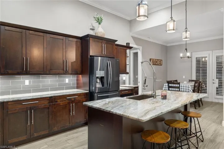 Kitchen with stainless steel fridge, light hardwood / wood-style floors, light stone countertops, and an island with sink