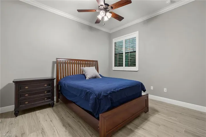 Bedroom featuring light wood-type flooring, ornamental molding, and ceiling fan