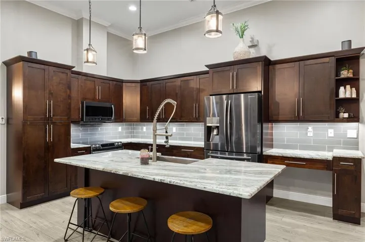 Kitchen featuring appliances with stainless steel finishes, pendant lighting, light stone counters, and light hardwood / wood-style flooring