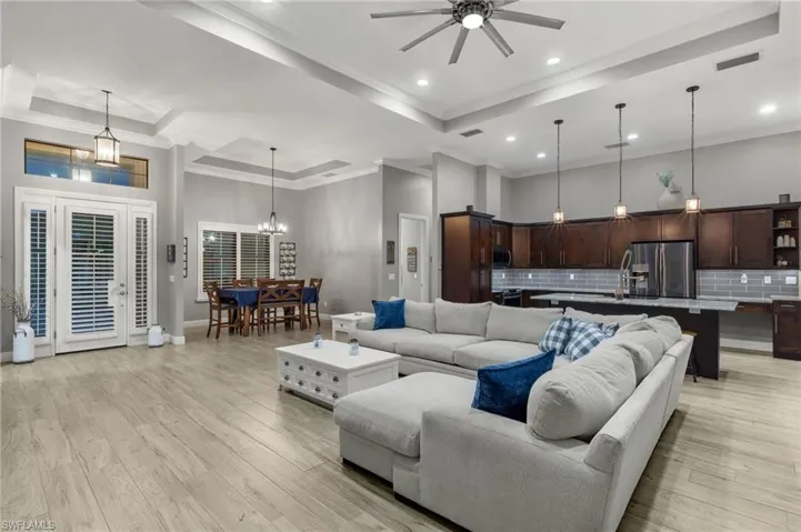 Living room featuring ceiling fan with notable chandelier, a high ceiling, ornamental molding, and light hardwood / wood-style flooring