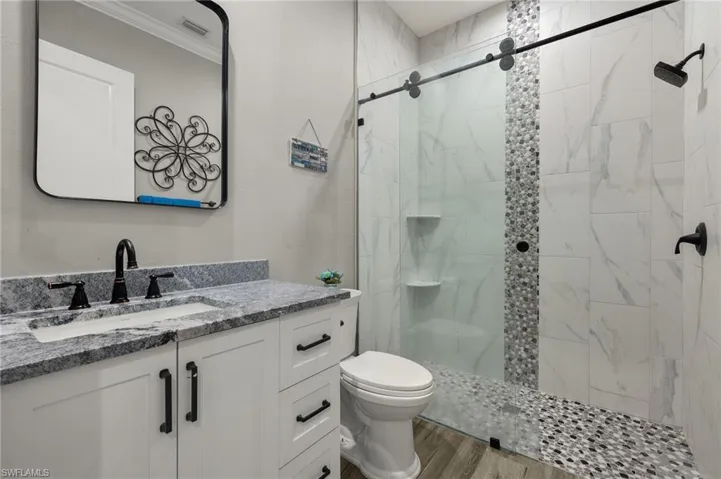 Bathroom featuring walk in shower, vanity, hardwood / wood-style floors, and toilet