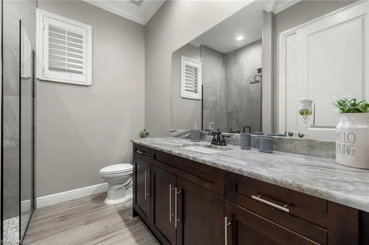 Bathroom featuring a shower with door, hardwood / wood-style floors, crown molding, vanity, and toilet