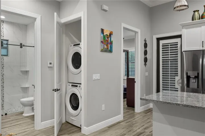 Laundry area featuring stacked washer and clothes dryer, ornamental molding, and light hardwood / wood-style flooring