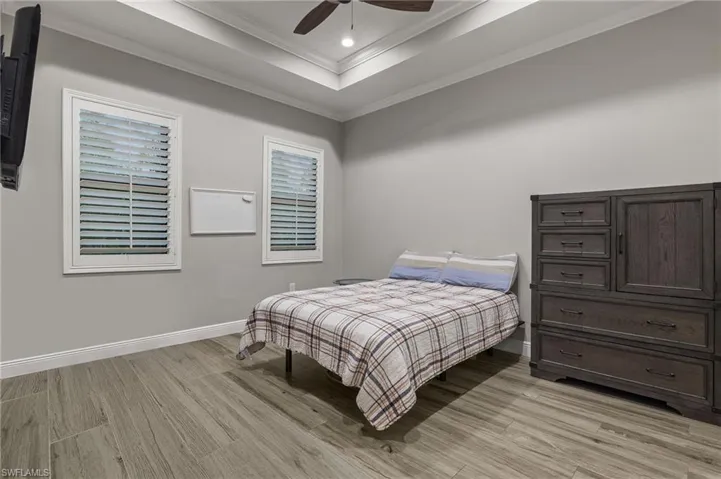 Bedroom featuring ceiling fan, light hardwood / wood-style floors, a raised ceiling, and ornamental molding