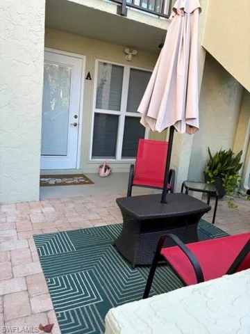 Private patio space featuring paver flooring, a white opaque glass entry door, and a multi-pane window with blinds