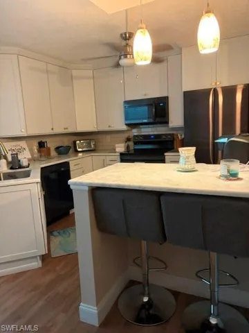 Kitchen featuring white shaker-style cabinetry, a light-toned backsplash, and a black appliance suite