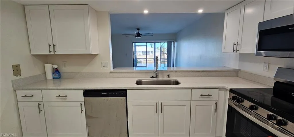 Kitchen with stainless steel appliances, white cabinetry, a ceiling fan, and light stone counters