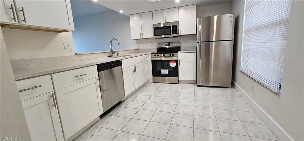 Kitchen with stainless steel appliances, white cabinetry, light stone countertops, light tile patterned floors, and recessed lighting
