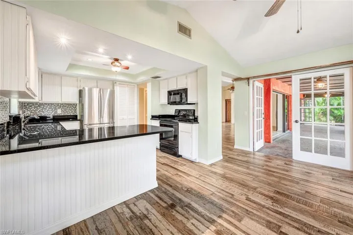 Kitchen featuring kitchen peninsula, tasteful backsplash, ceiling fan, black appliances, and white cabinets