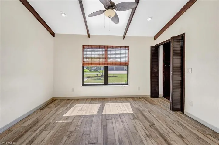 Unfurnished bedroom with ceiling fan, lofted ceiling with beams, and light hardwood / wood-style floors