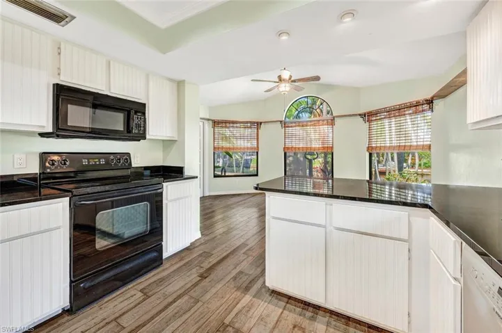 Kitchen with light hardwood / wood-style flooring, kitchen peninsula, ceiling fan, black appliances, and lofted ceiling