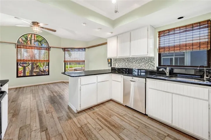 Kitchen featuring ceiling fan, light hardwood / wood-style floors, kitchen peninsula, stainless steel dishwasher, and white cabinetry