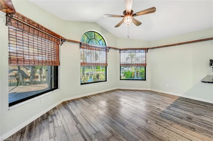 Empty room with a healthy amount of sunlight, ceiling fan, vaulted ceiling, and hardwood / wood-style floors
