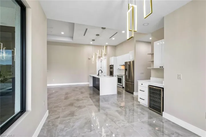 Kitchen with wine cooler, an island with sink, stainless steel appliances, sink, and white cabinetry