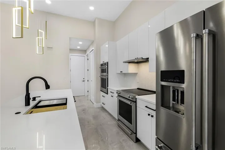 Kitchen with white cabinetry, high end appliances, sink, tasteful backsplash, and light tile floors