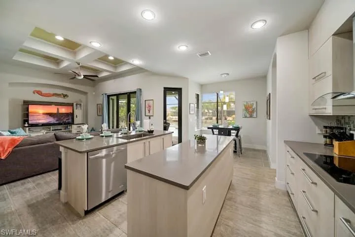 Kitchen featuring sink, white cabinetry, a center island with sink, stainless steel dishwasher, and black electric stovetop