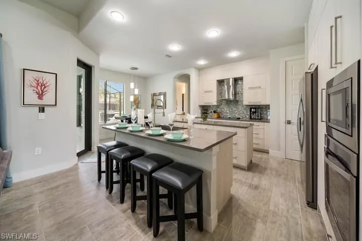 Kitchen featuring a breakfast bar area, white cabinetry, a center island with sink, stainless steel appliances, and backsplash