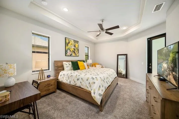 Bedroom with light colored carpet, ceiling fan, and a tray ceiling