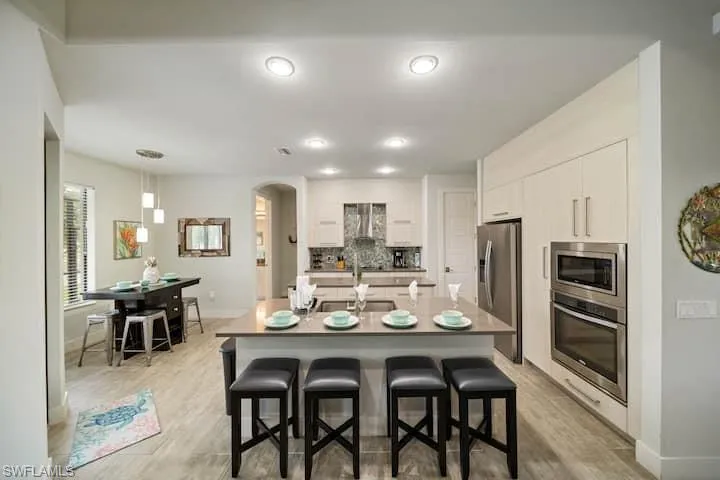Kitchen featuring white cabinets, a kitchen bar, hanging light fixtures, a kitchen island with sink, and stainless steel appliances