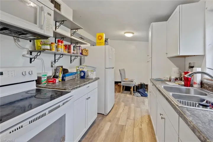 Kitchen featuring light hardwood / wood-style floors, white cabinetry, sink, and white appliances
