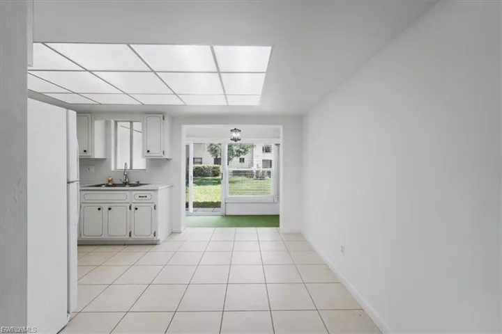 Kitchen with freestanding refrigerator, light tile patterned flooring, white cabinetry, decorative backsplash, and light countertops