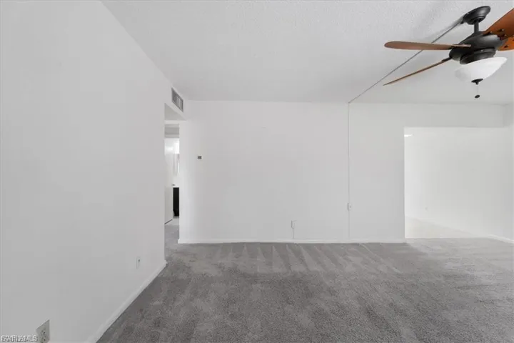Empty room with light colored carpet, a ceiling fan, and a textured ceiling