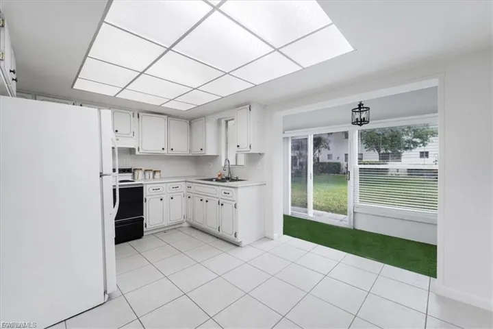 Kitchen with freestanding refrigerator, backsplash, light countertops, light tile patterned flooring, and range with electric stovetop