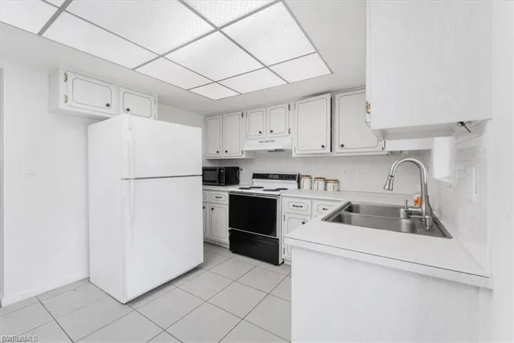Kitchen featuring white appliances, light countertops, tasteful backsplash, and white cabinetry